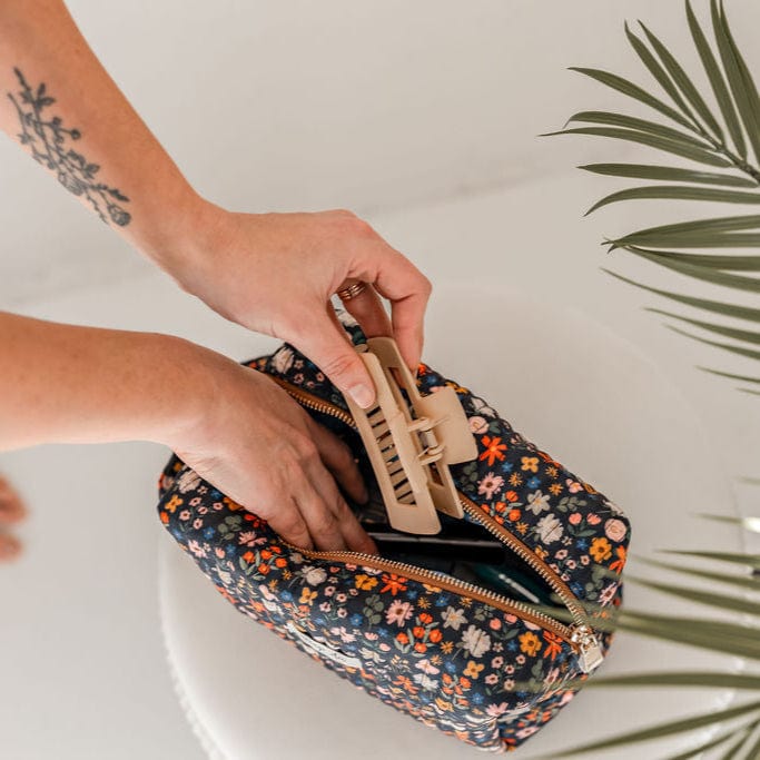 Woman's hands reaching into floral cosmetic bag, holding hair clip.