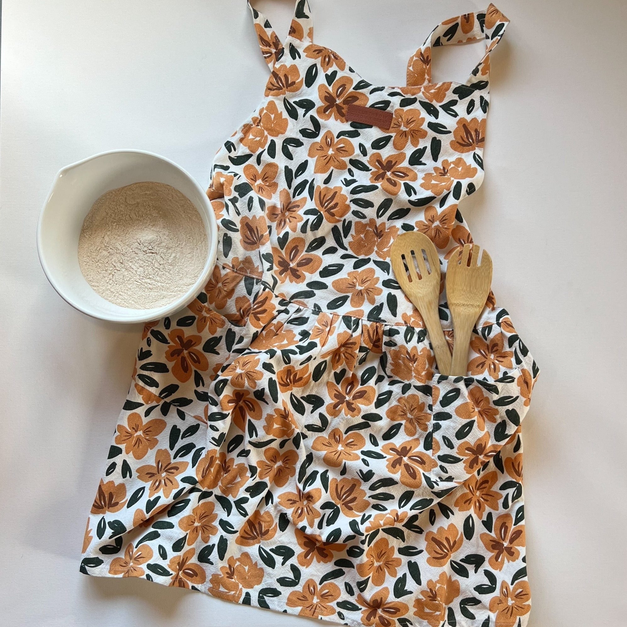 Floral apron with flour and wooden utensils.