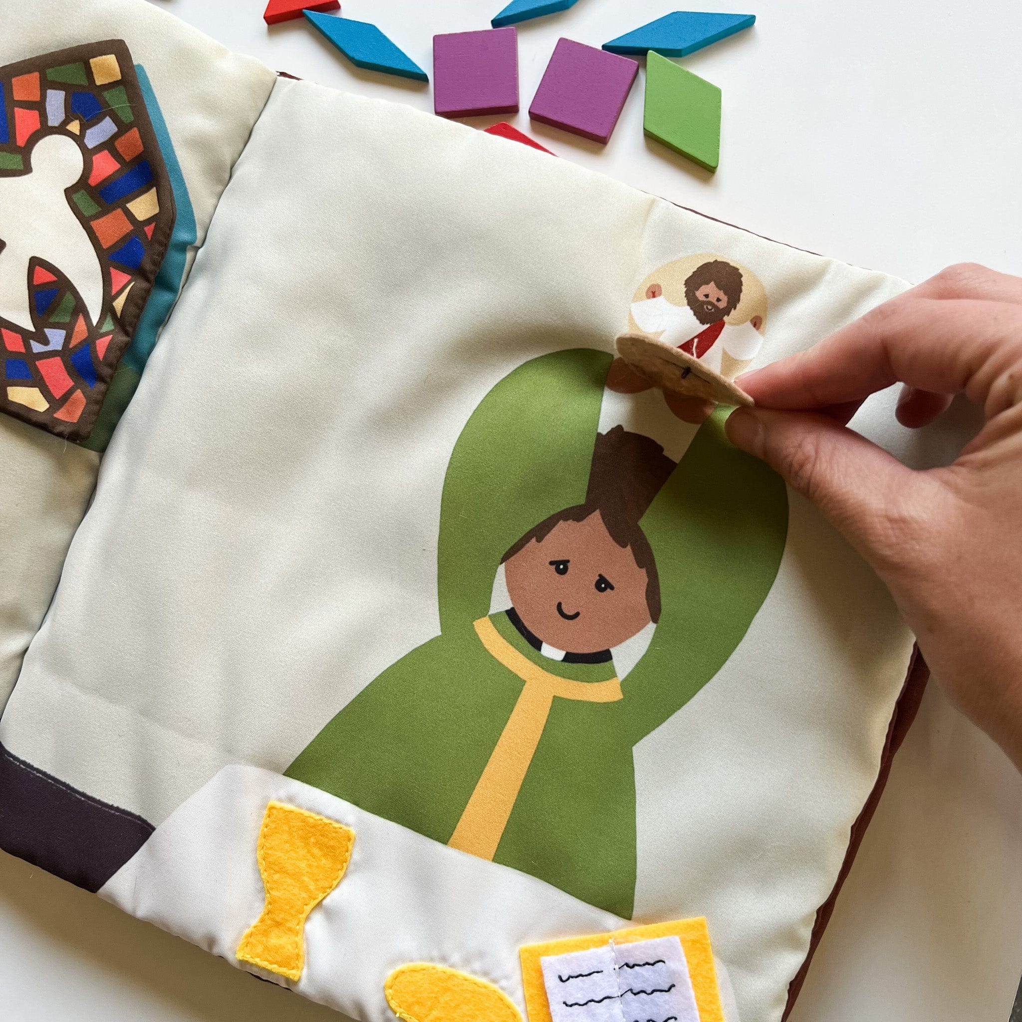 Fabric book with a priest illustration and wooden figure.
