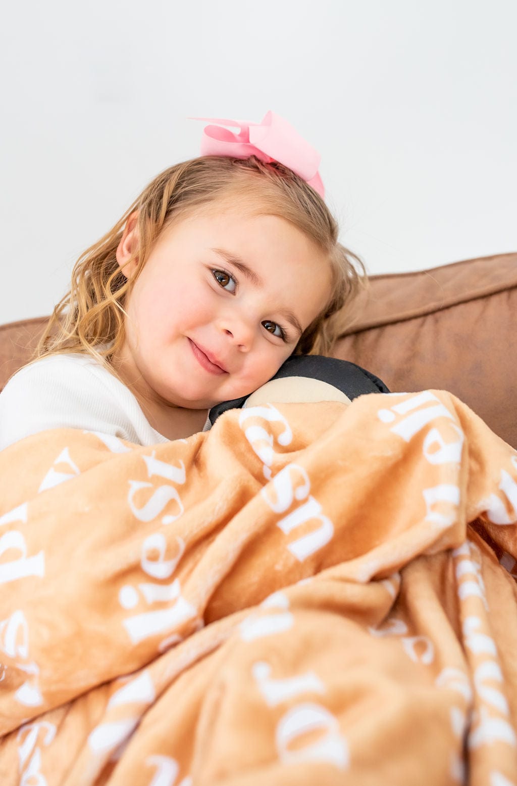 Girl with pink bow holding a blanket and toy.