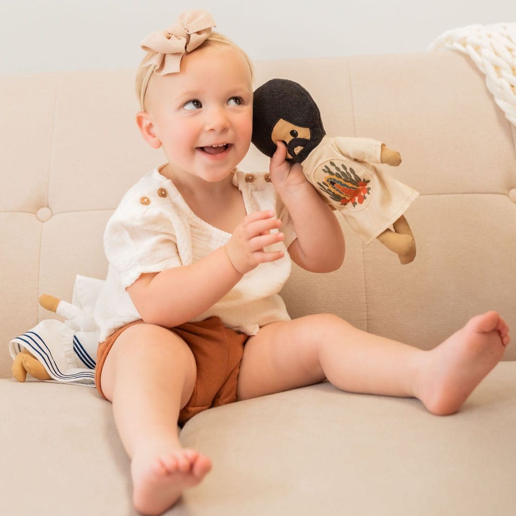 Toddler holding a doll on a couch.