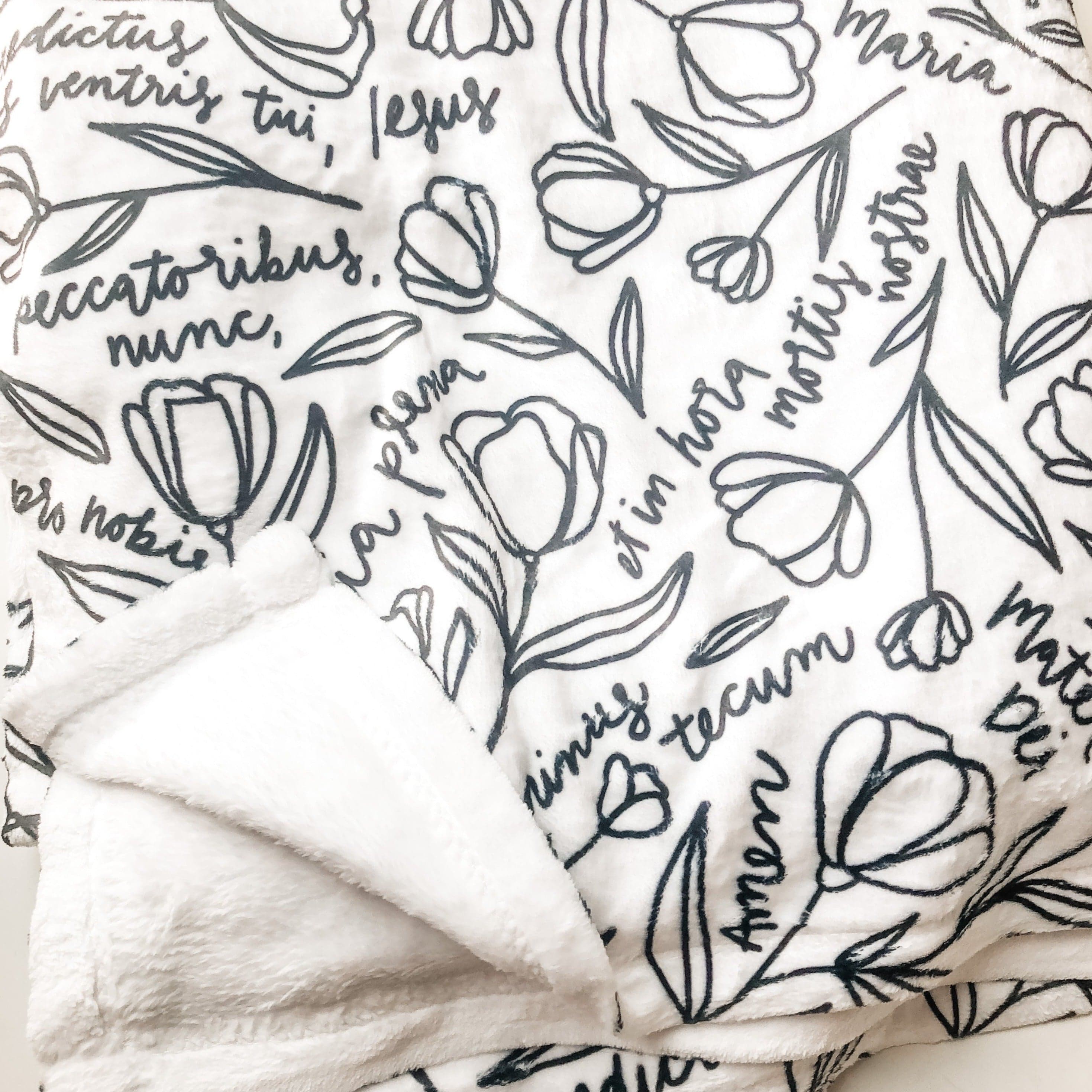 White blanket with black floral design and script.