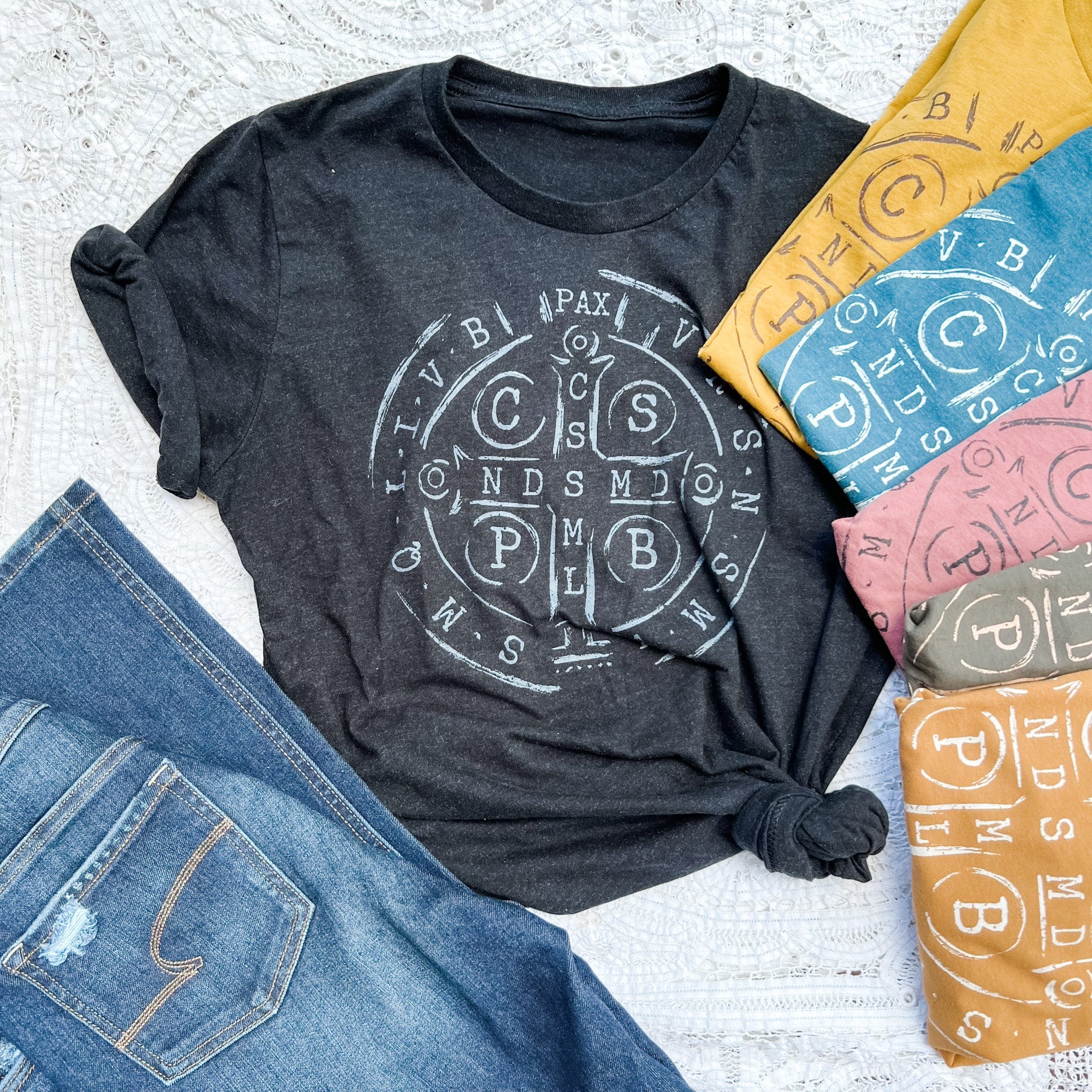 Black t-shirt with design and jeans, stacked colorful t-shirts.