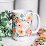 White mug with floral design and religious text.