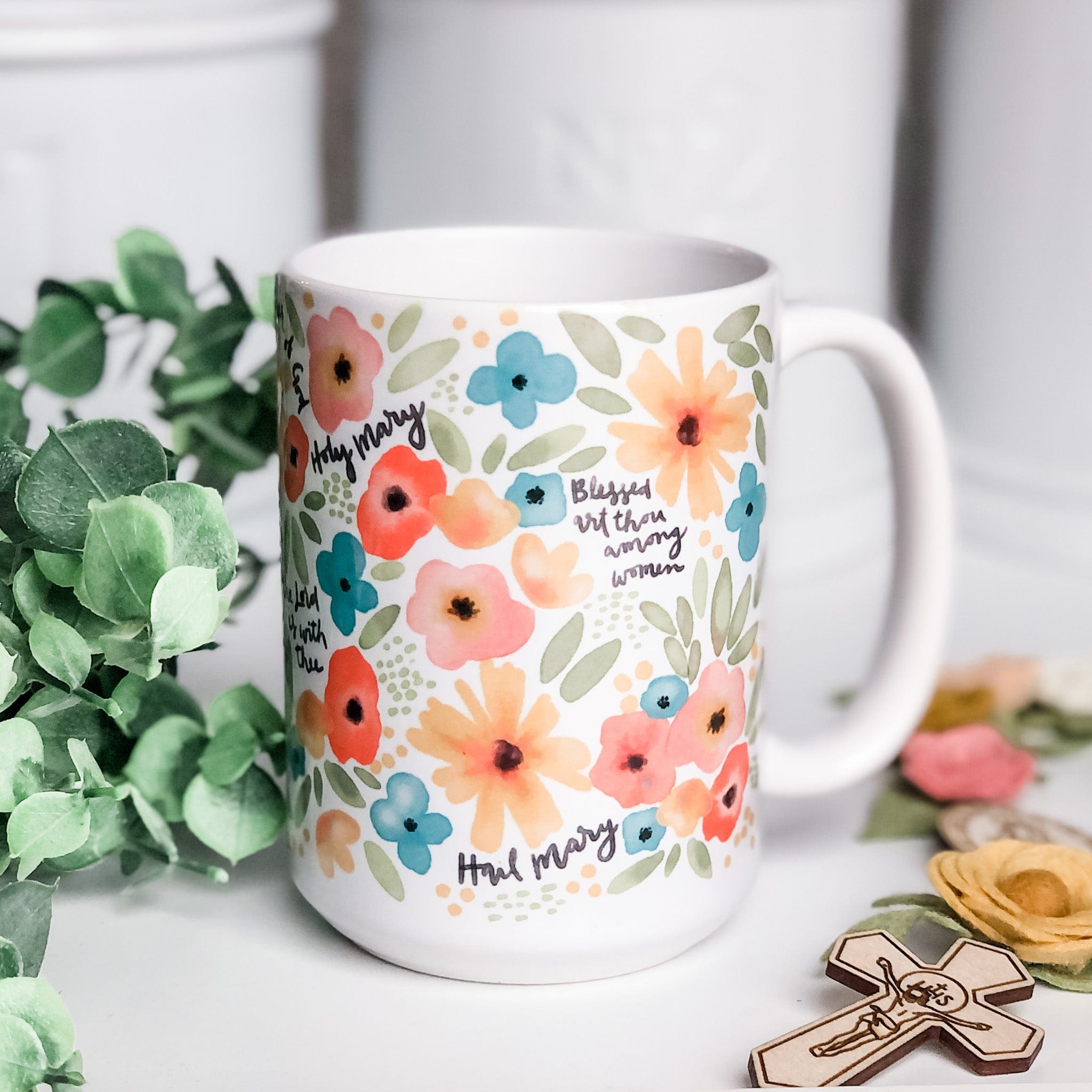 White mug with floral design and religious text.