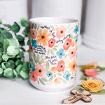 Floral-patterned mug with text and wooden cross.
