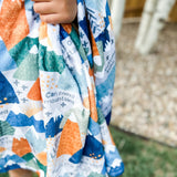 Child holding a patterned blanket with mountain design.
