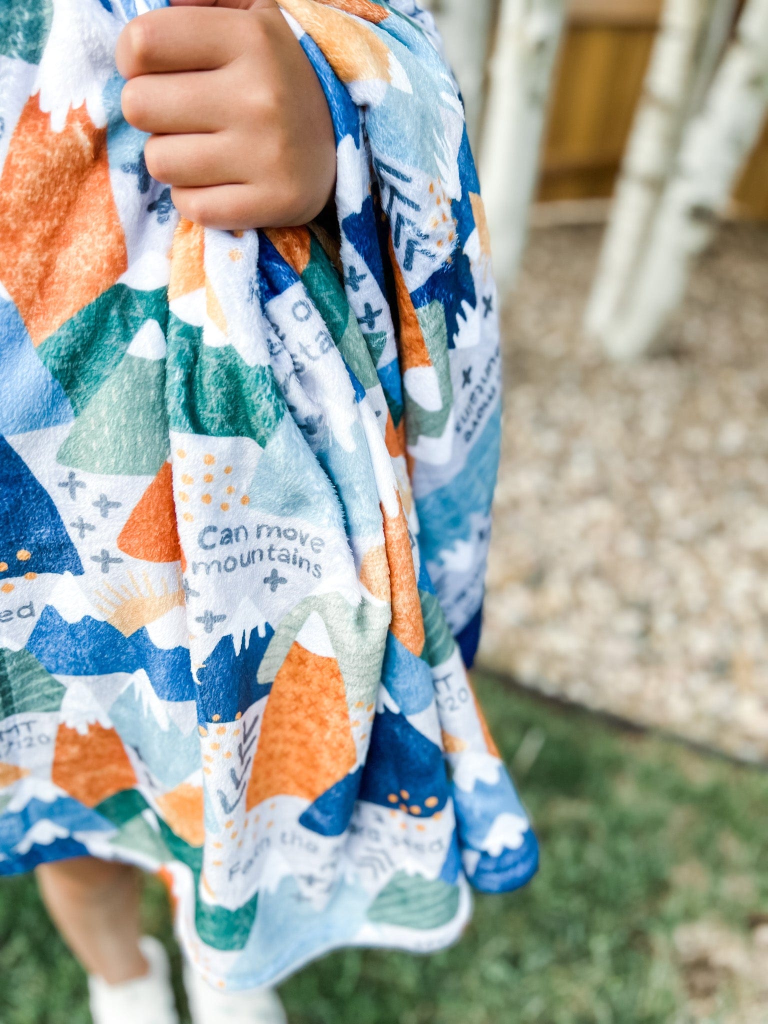 Child holding a patterned blanket with mountain design.