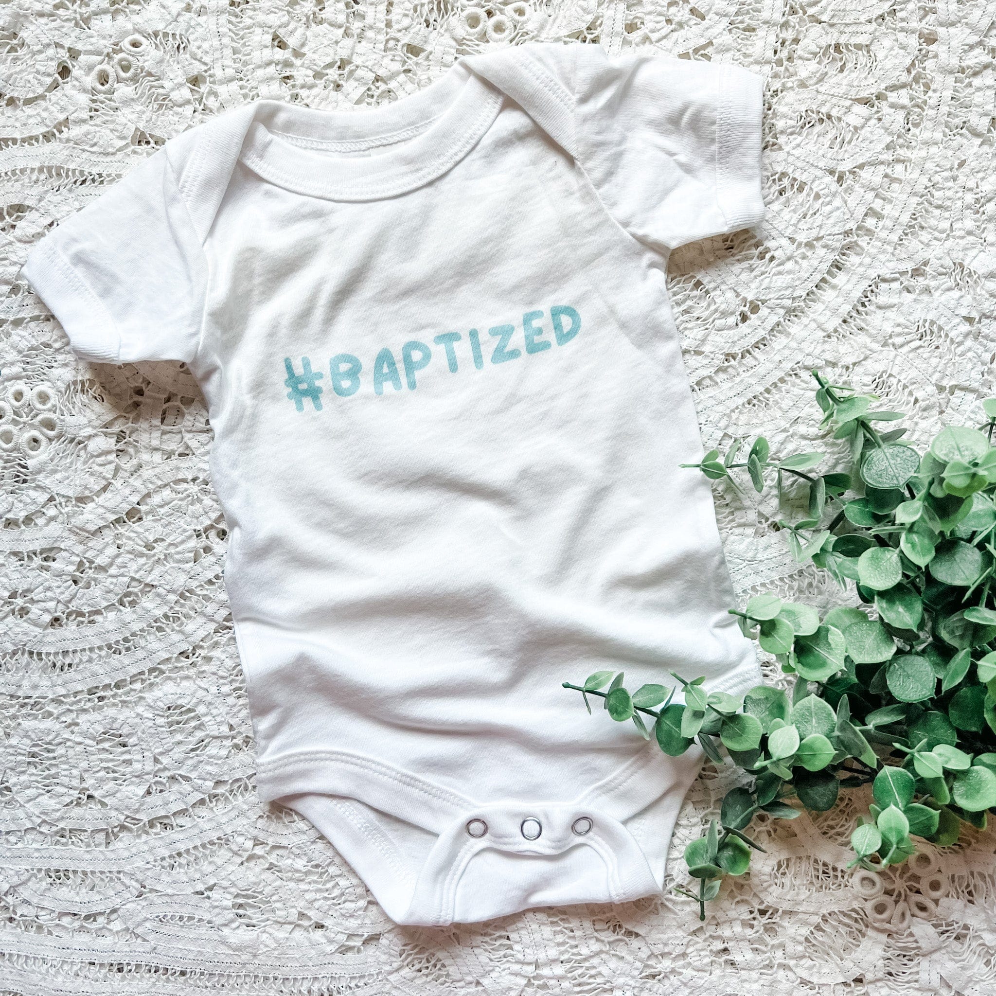 White baby onesie with #BAPTIZED text.