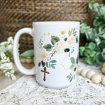 White mug with floral design and cross.