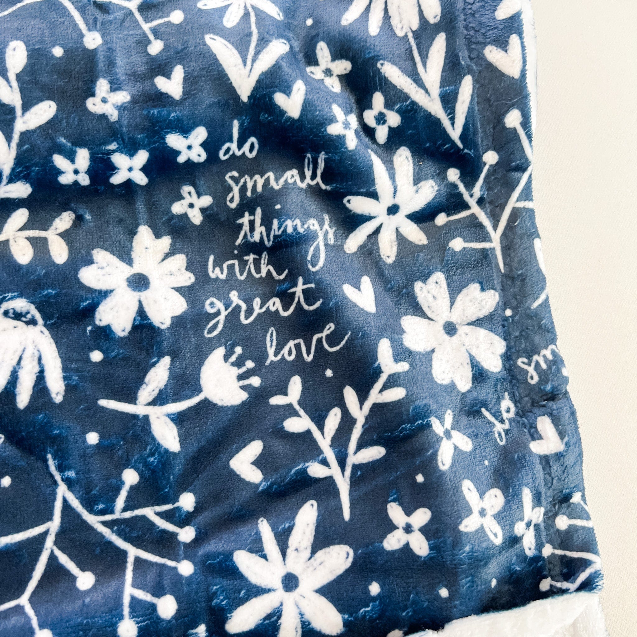 Blue blanket with white floral pattern and quote.