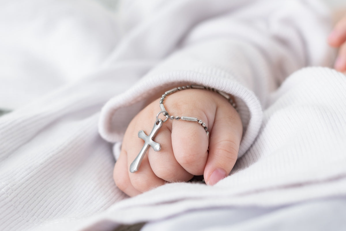 Best Catholic baby gifts featuring baby hand with cross bracelet.