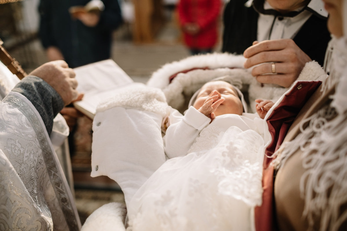 Catholic baptism ceremony with priest blessing infant in white gown, illustrating what is an appropriate gift for a Catholic baptism.
