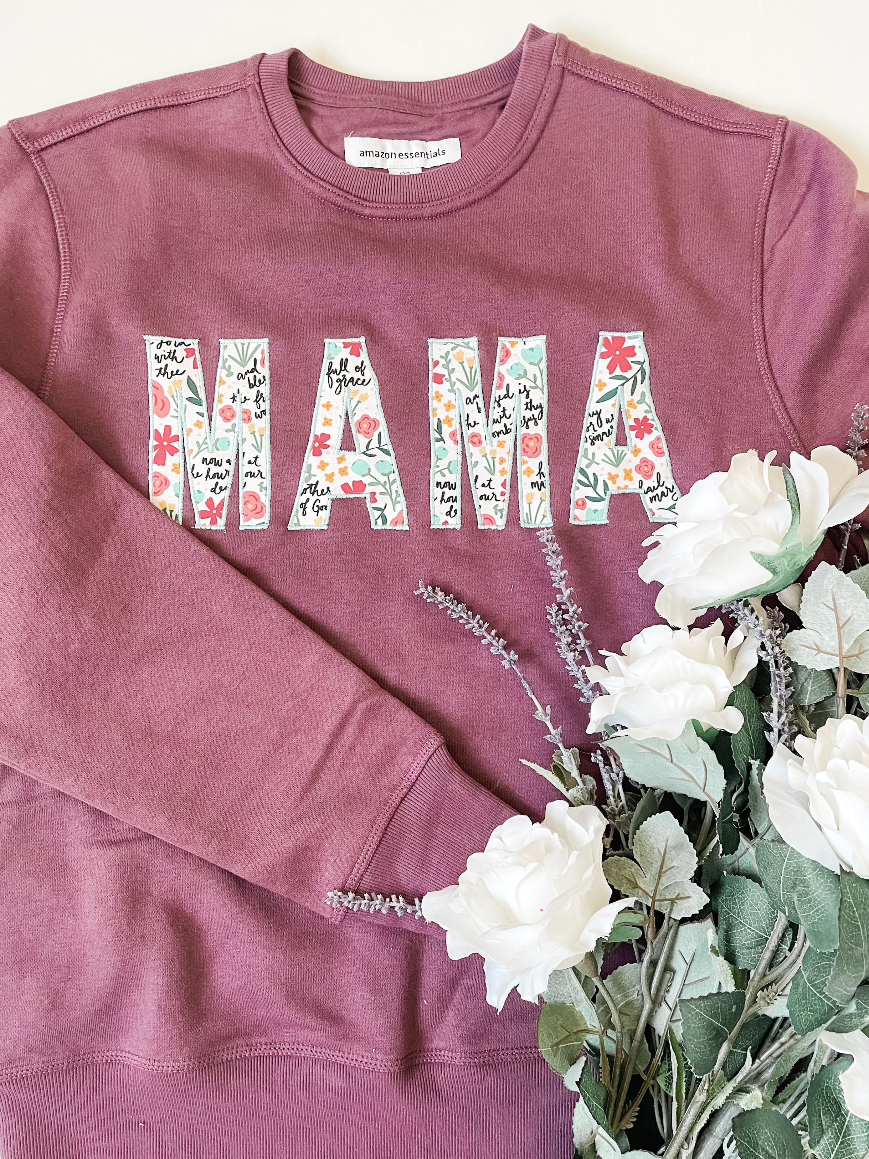 Flat lay of handmade “Mama” embroidered sweatshirt made with Catholic Hail Mary Floral fabric — a modern faith-inspired sewing project for moms.