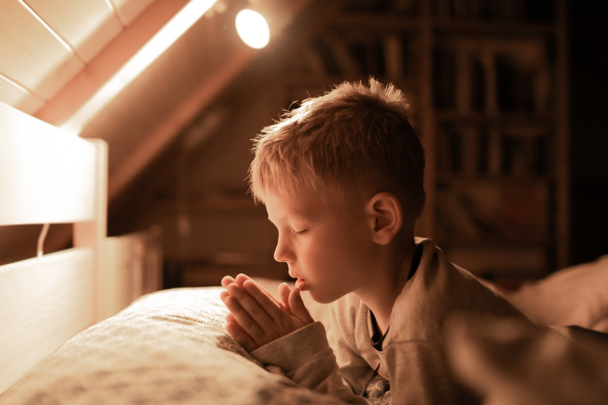 Young boy praying in bedroom while thinking of the best first communion gifts.