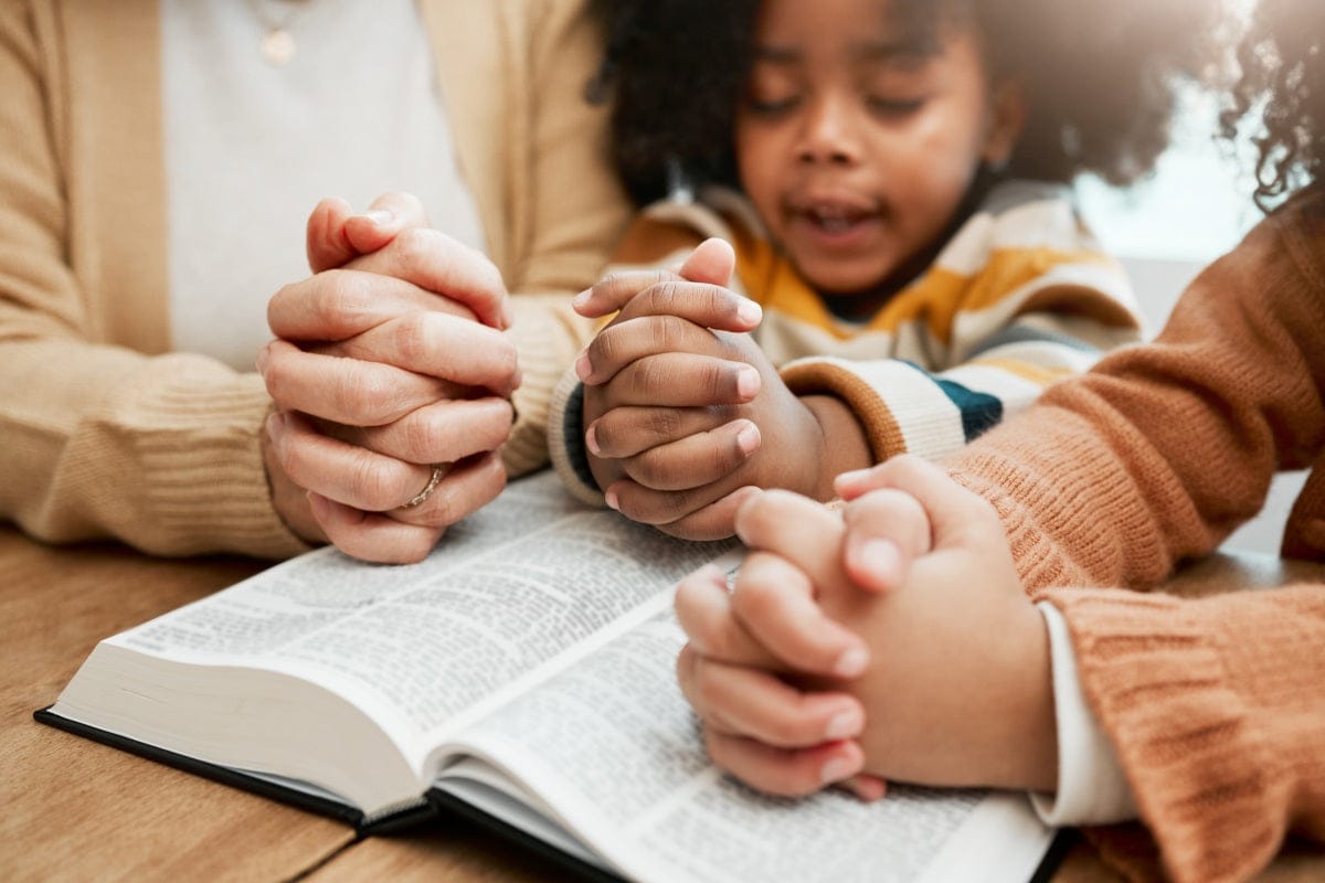 Parents and daughter praying over a bible while considering first communion gifts