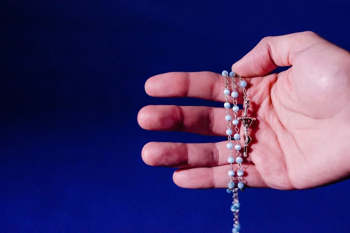 hand holding a pretty blue and silver Rosary for learning how to pray the Rosary