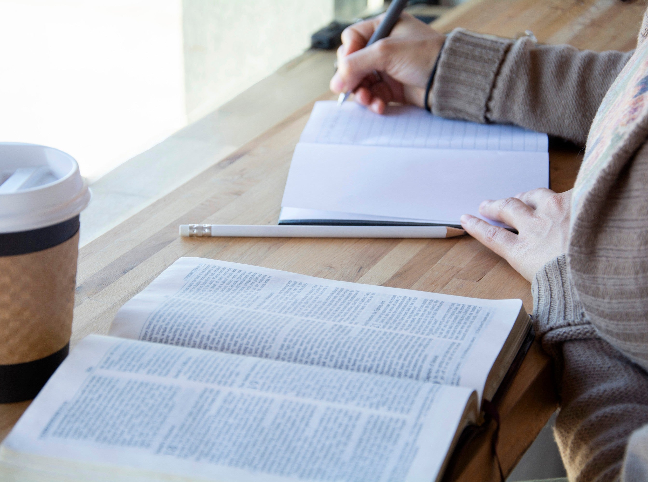 woman showcasing how to organize a prayer journal by journaling while reading the Bible in a coffee shop