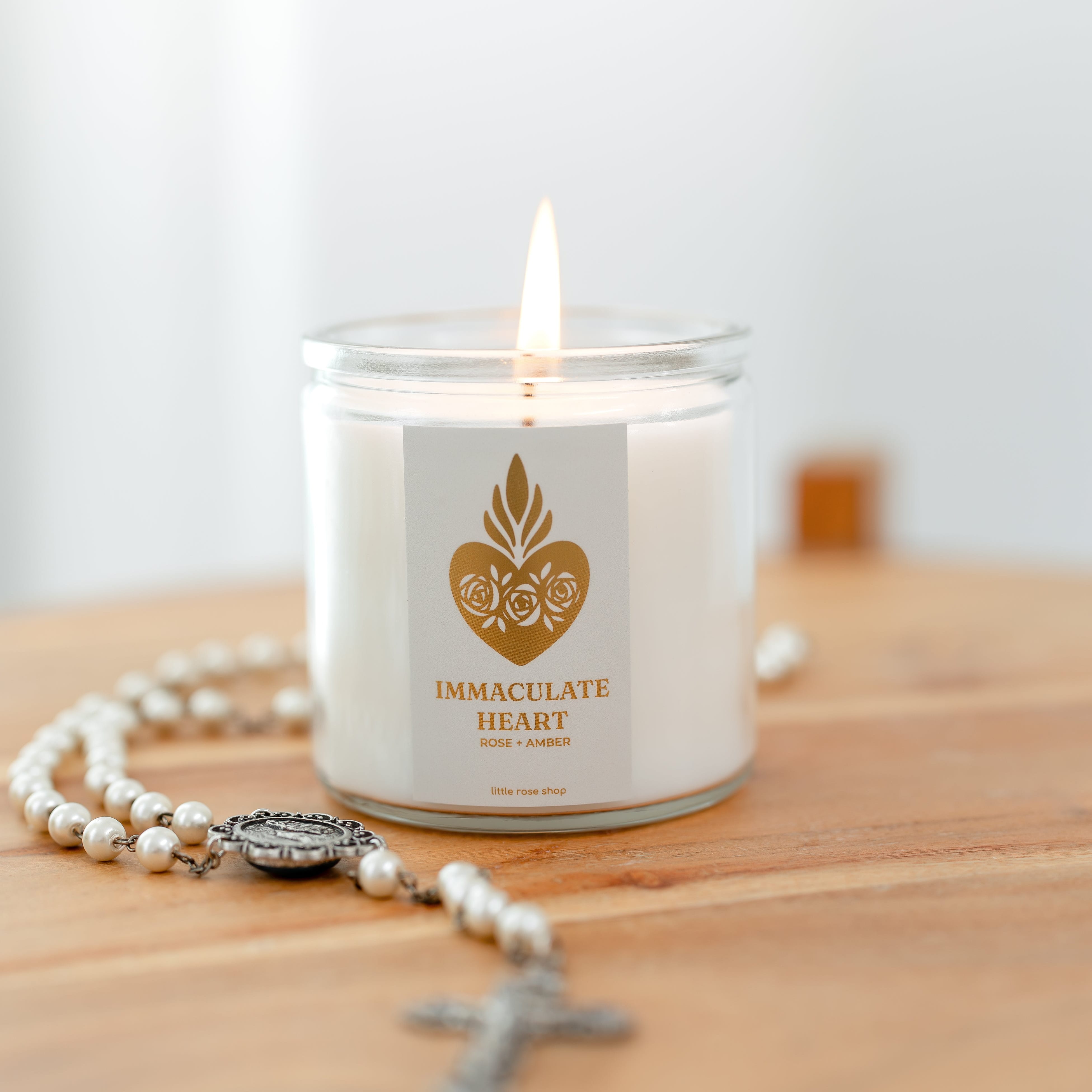 Candle labeled 'Immaculate Heart' with a rosary on a wooden surface