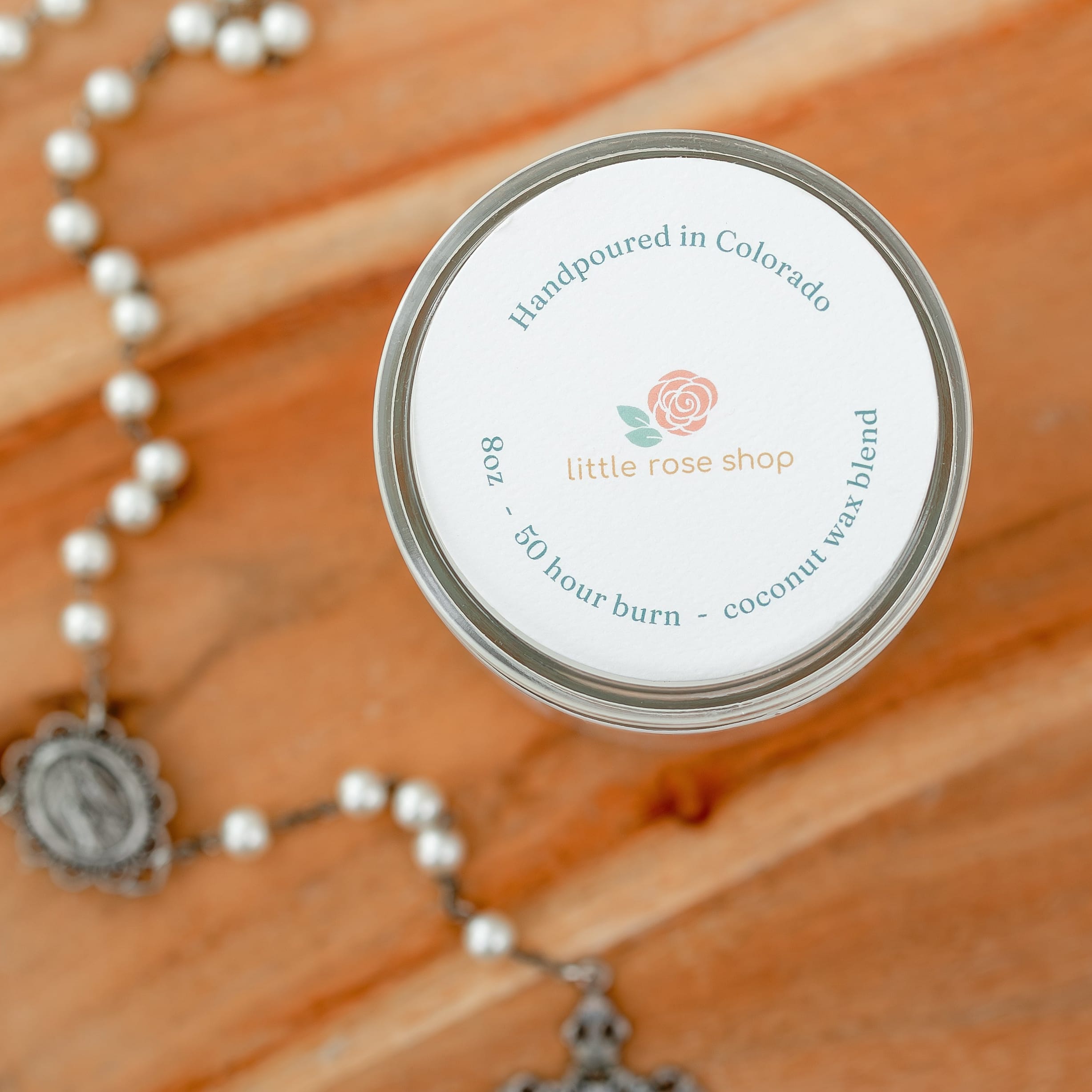 Small round container with a label on a wooden surface next to a rosary