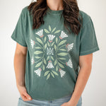 Person wearing a green t-shirt with floral design and jeans on a plain background