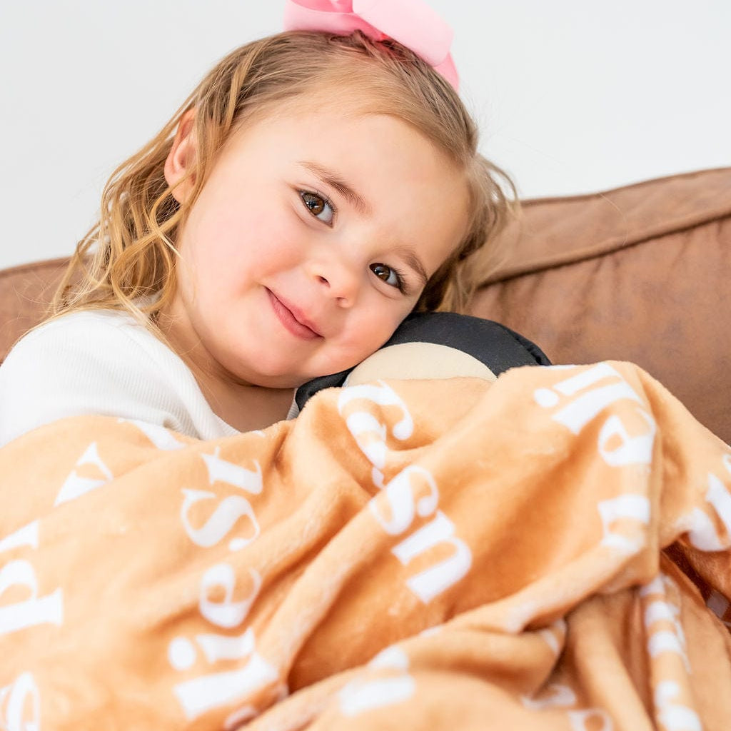 Girl with pink bow holding a blanket and toy.