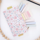 Floral pencil case with stationery items on a white surface