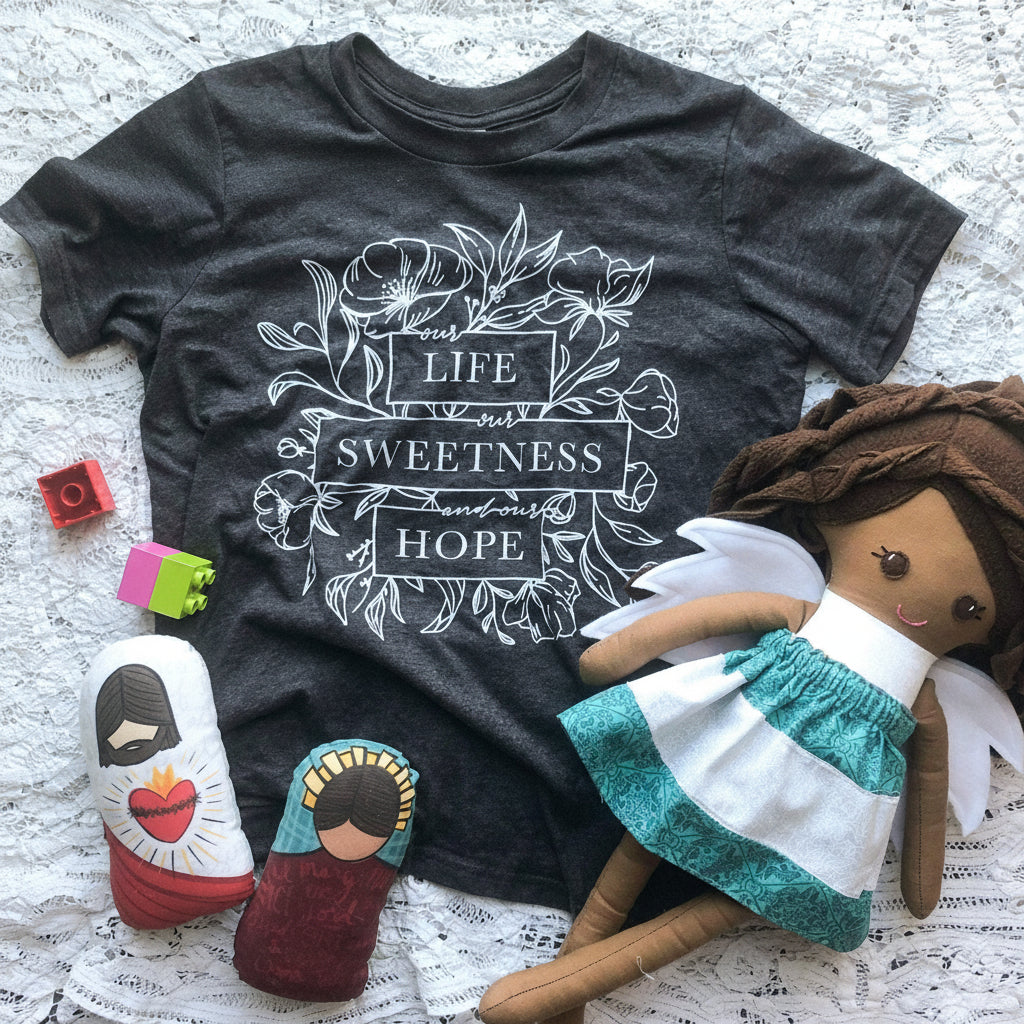 Youth shirt, doll, blocks, and religious toys on a blanket.