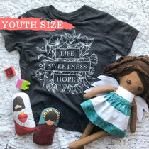 Youth shirt, doll, blocks, and religious toys on a blanket.